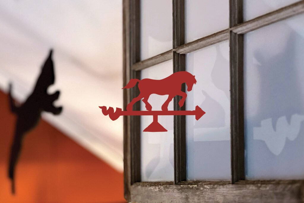 Red horse-shaped weather vane with an old wooden window in background